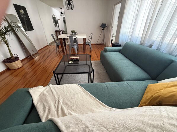 Ein Wohnzimmer mit einer Couch, einem Couchtisch, einem Esstisch mit Stühlen, einer Stehlampe und einer Topfpflanze.