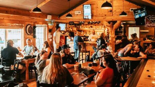 Um interior rústico de madeira com área de bar, mesas e cadeiras.