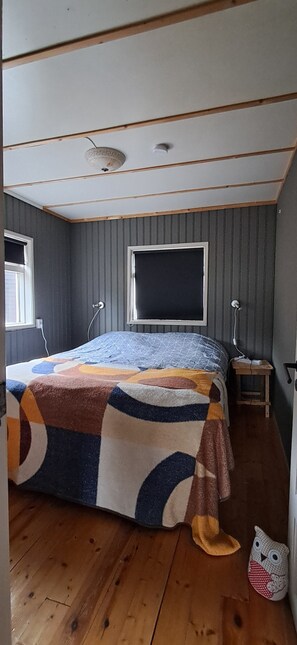 Ein Schlafzimmer mit einem Bett, das mit einer farbenfrohen Steude bezogen ist, einem Holzboden, einem Fenster und einem kleinen Nachttisch mit einer Lampe.
