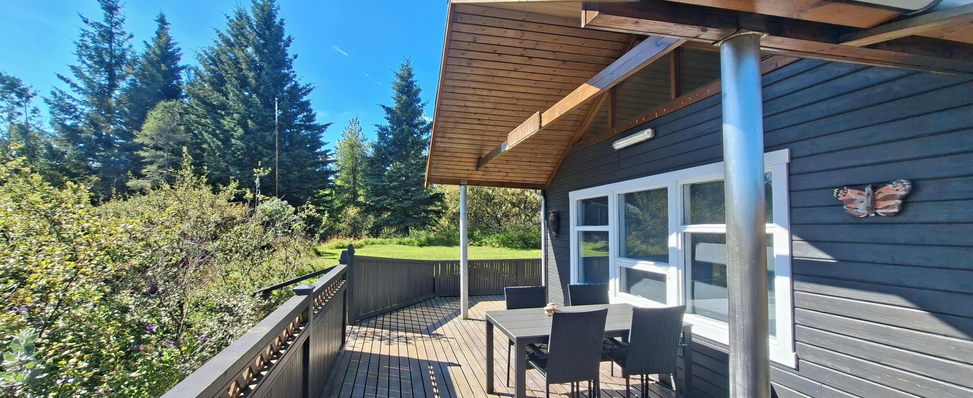 A wooden deck with outdoor furniture, a covered area with a roof, and a view of a forested area.