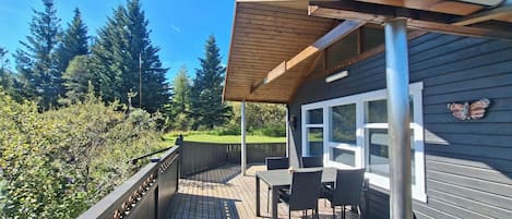 A wooden deck with outdoor furniture, a covered area with a roof, and a view of a forested area.