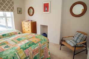 A bedroom with two beds, a wooden dresser, a wicker chair, and wall-mounted mirrors.
