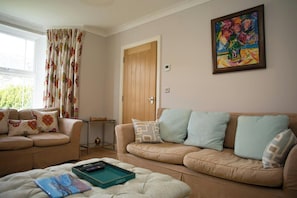A living room with a beige sofa, a coffee table with a remote control, and a painting on the wall.