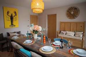 A dining area with a wooden table set for four, a wall clock, and a lobster painting. - Green Meadows, Newport (Newport)