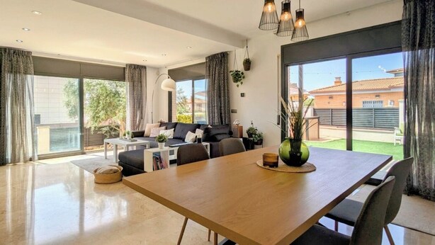 Amplia sala de estar con una mesa de comedor de madera, un conjunto de sofás y un gran ventanal corredera que da a un balcón.