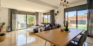 Un vaste espace de vie comprenant une table à manger en bois, un ensemble de canapés et une grande porte-fenêtre coulissante donnant sur un balcon.