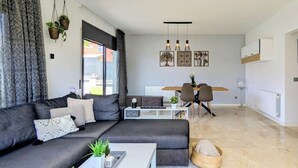 Una sala de estar moderna con un sofá gris, una mesa de centro blanca y un comedor con una mesa y sillas.