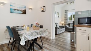 A dining area with a table set for four, a kitchen with a microwave, and a living area with a sofa and a TV. - Fern Cottage - Dog Friendly Cottage With Hot Tub (Kilgetty)