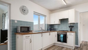 A modern kitchen with white cabinets, a microwave, a stove, and a sink. - Fern Cottage - Dog Friendly Cottage With Hot Tub (Kilgetty)