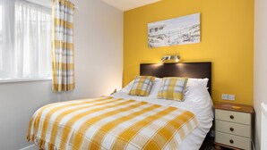 A bedroom with a bed, a nightstand, a lamp, and a painting on the wall. - Fern Cottage - Dog Friendly Cottage With Hot Tub (Kilgetty)