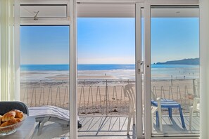 A room with a view of a beach, a table with a bowl of croissants, and a chair. - 9 Strandways - Sea Views Parking Beach Access (Saundersfoot)
