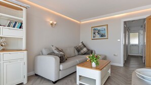 A modern living room with a sofa, a coffee table, a bookshelf, and a painting on the wall. - 9 Strandways - Sea Views Parking Beach Access (Saundersfoot)