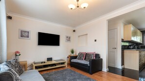 Un salon avec un canapé gris, un canapé noir, un téléviseur à écran plat, une table basse en bois et un tapis gris.