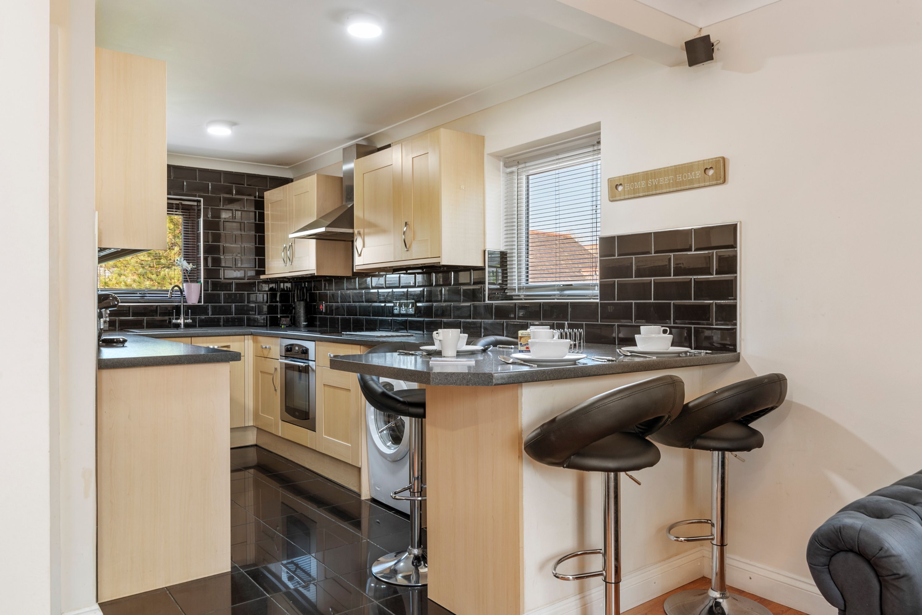 A modern kitchen with a central island, bar stools, and a window with blinds.