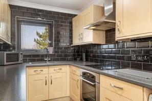 A modern kitchen with black tiled backsplash, stainless steel appliances, and light wood cabinetry. - Little Haven - Cosy Tenby Apartment (Tenby)