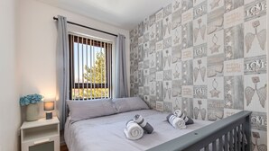 Une chambre à coucher avec un lit, une table de chevet, une fenêtre avec des rideaux et un mur orné d’un motif.
