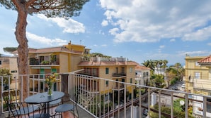 Ein Balkon mit Tisch und Stühlen, der auf ein Wohngebiet mit mehreren Gebäuden und einem klaren Himmel blickt.