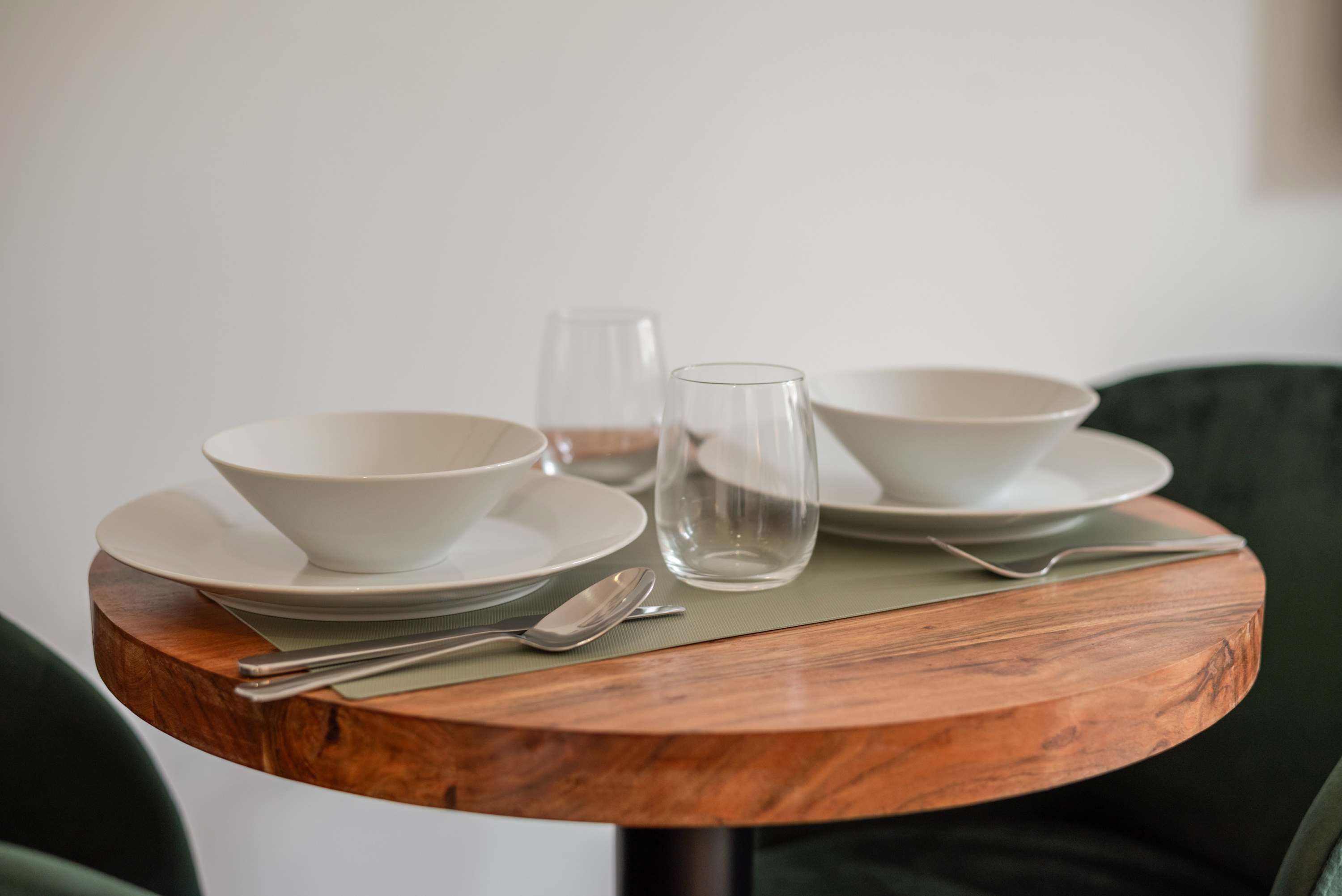 A round wooden table with white bowls, a glass, and cutlery.