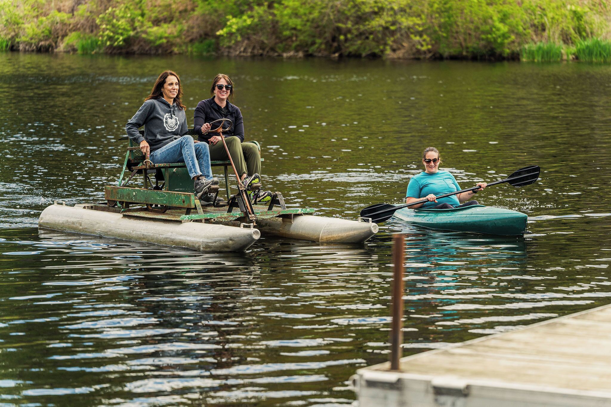 Two people on a small boat and one person kayaking nearby.