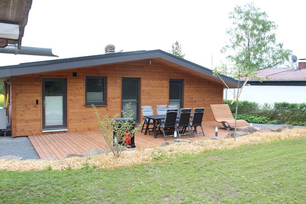A modern wooden house with a deck, a sliding door, and a patio with outdoor furniture.