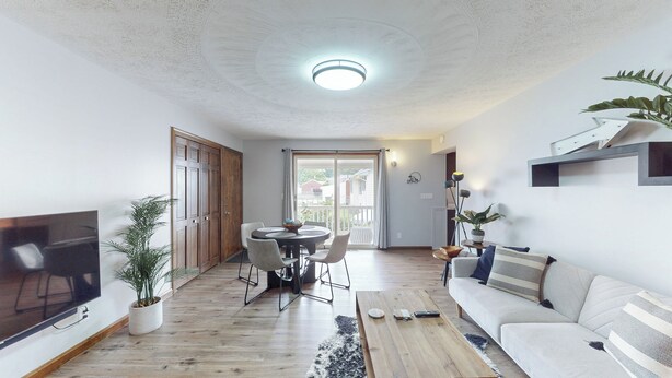 A living room with a wooden floor, a sofa, a coffee table, and a TV. There is a dining area with a table and chairs. - Snap, Set, Stay- Game Day Comfort Near It All (Canton)