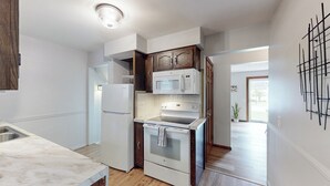 A modern kitchen with white appliances, wooden cabinets, and a marble countertop. - Snap, Set, Stay- Game Day Comfort Near It All (Canton)