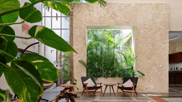 An indoor pool area with wooden loungers, a stone wall, and a view of lush greenery outside. - WAYAK Luxury! 5BR Private Pool & Gym, 24/7Security (Tulum)