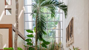 A modern interior with a grey sofa, a wooden table with a bottle and glasses, and tropical plants. - WAYAK Luxury! 5BR Private Pool & Gym, 24/7Security (Tulum)