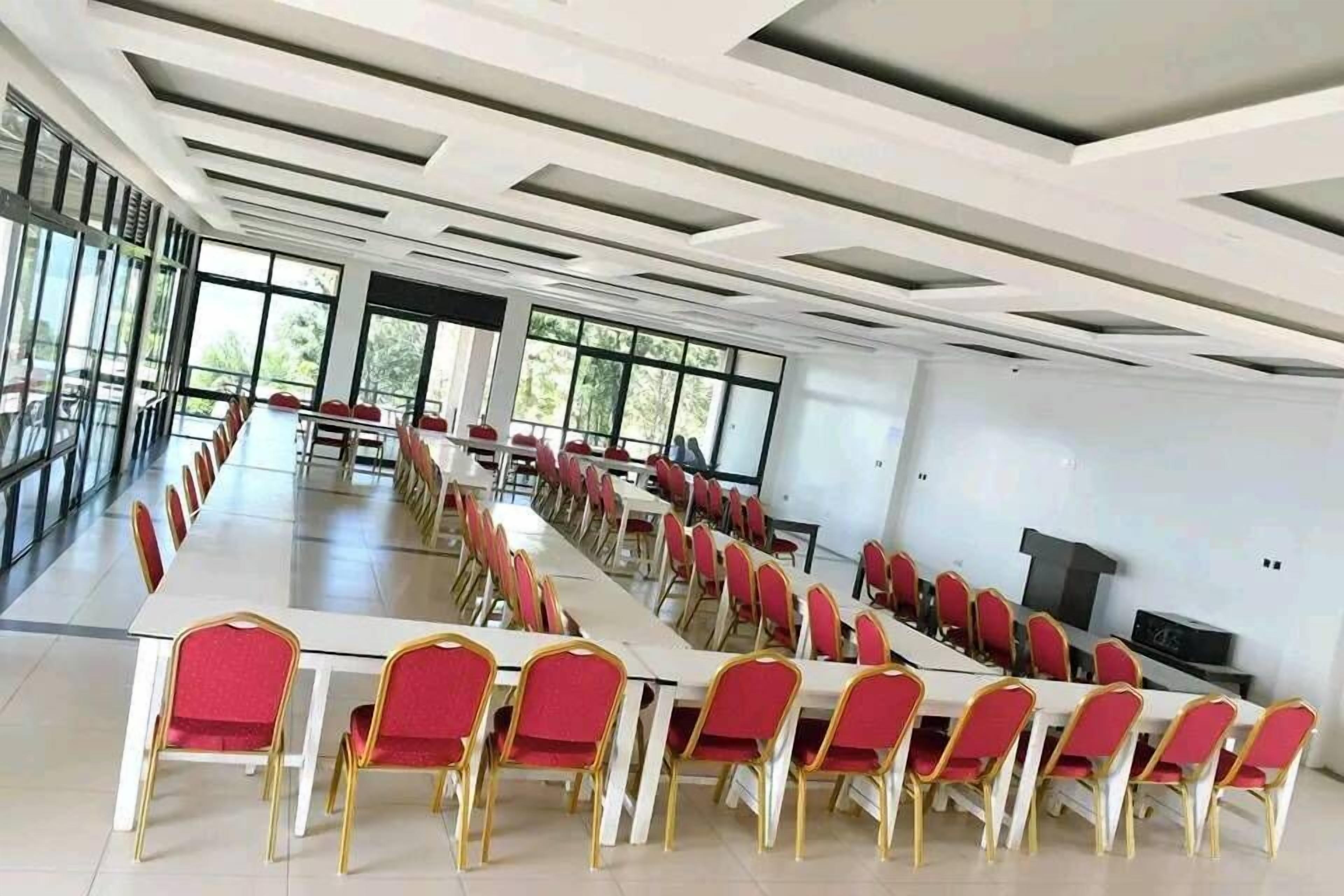 Une salle de conférence dotée de longues tables et de chaises rouges, de grandes fenêtres et d’un plafond au design moderne.