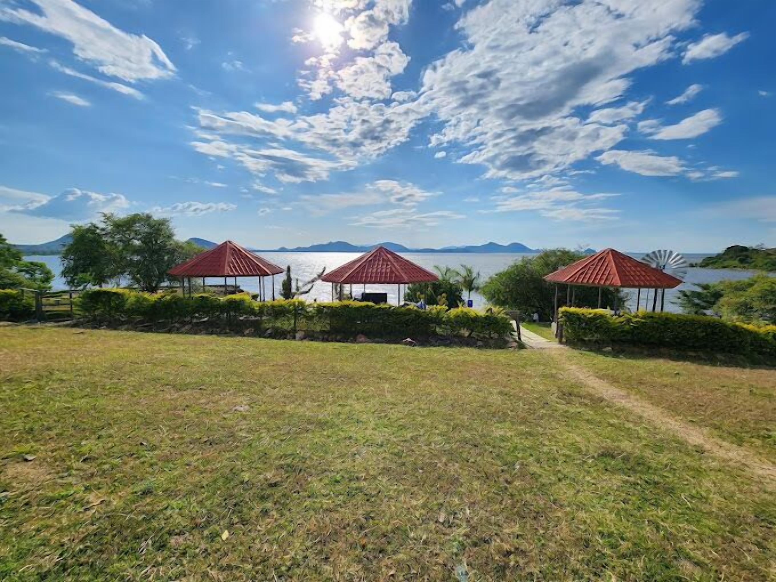 A grassy area with three red-roofed gazebos, a path leading to them, and a body of water in the background.