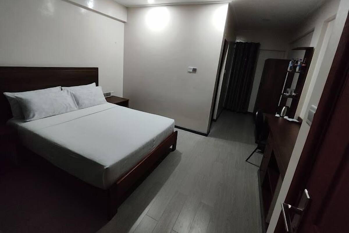 Una camera d'albergo con un letto, un comodino, un armadio e un bagno visibile tramite una porta.
