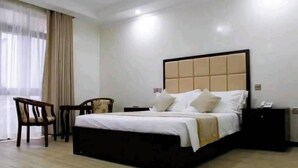 Hotellihuone, jossa on suuri sänky, yöpöytä, tuoli ja ikkuna, jossa on verhot.