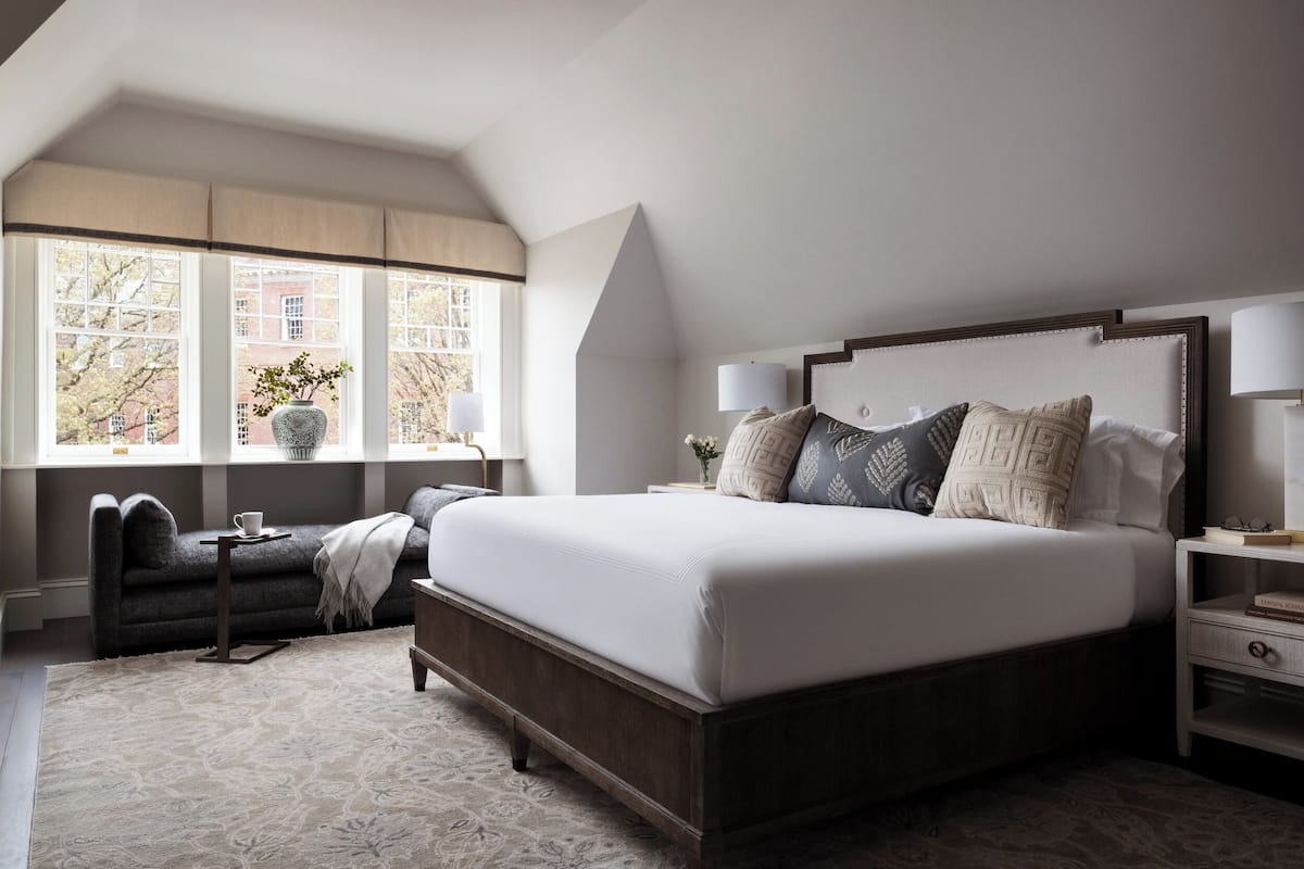 Une chambre avec un grand lit, une table de chevet, une commode, une fenêtre donnant sur des immeubles et un canapé.