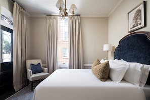 A hotel room with a large bed, a chair, a chandelier, and a window with curtains. - 86 State Circle - Luxury Boutique Hotel (Annapolis)