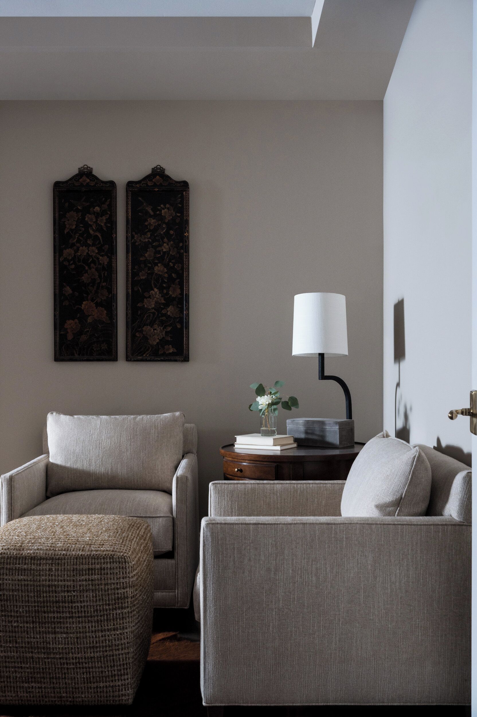 A living room with two armchairs, a small table with a lamp, and two wall-mounted paintings.