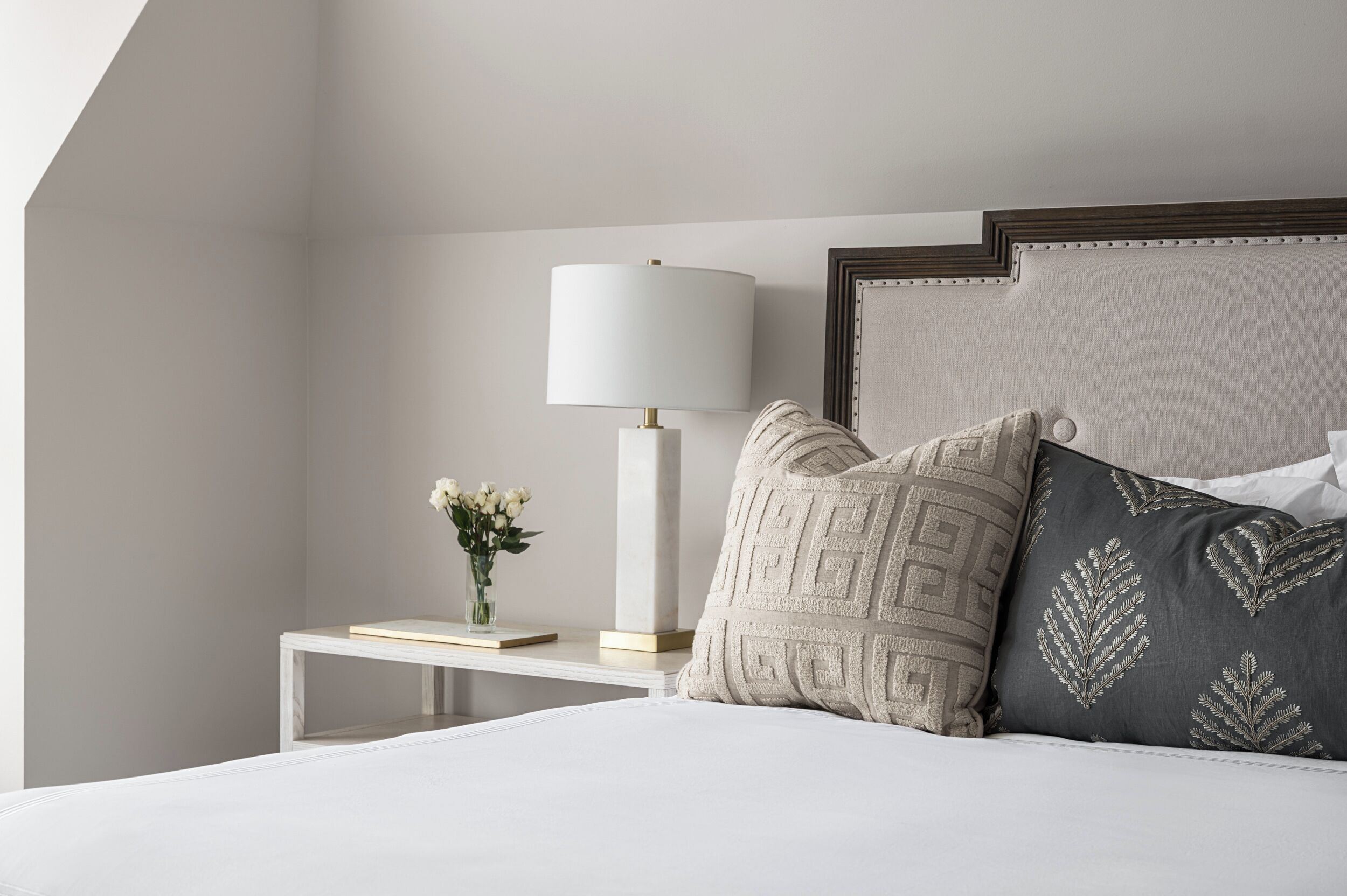 Une chambre à coucher bien rangée, avec un lit, une table de chevet dotée d’une lampe et des coussins décoratifs.