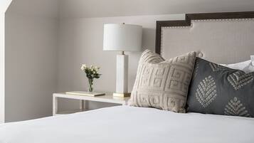 Une chambre à coucher bien rangée, avec un lit, une table de chevet dotée d’une lampe et des coussins décoratifs.