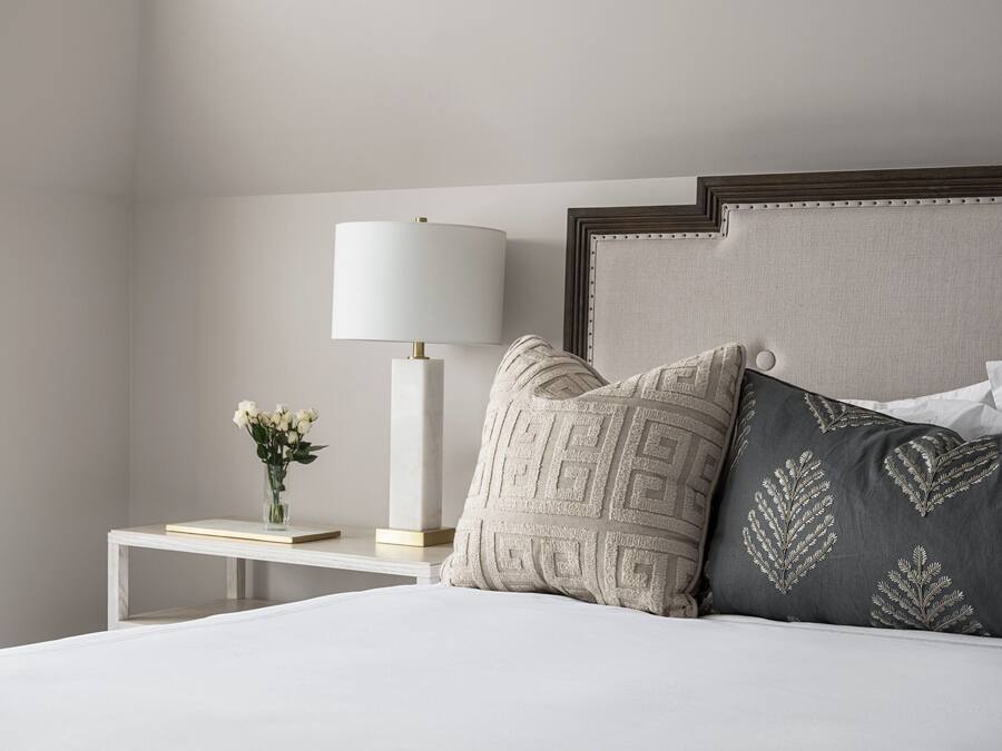 Une chambre à coucher bien rangée, avec un lit, une table de chevet dotée d’une lampe et des coussins décoratifs.