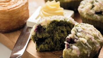 A wooden cutting board with a green muffin, a knife, and a container of butter.