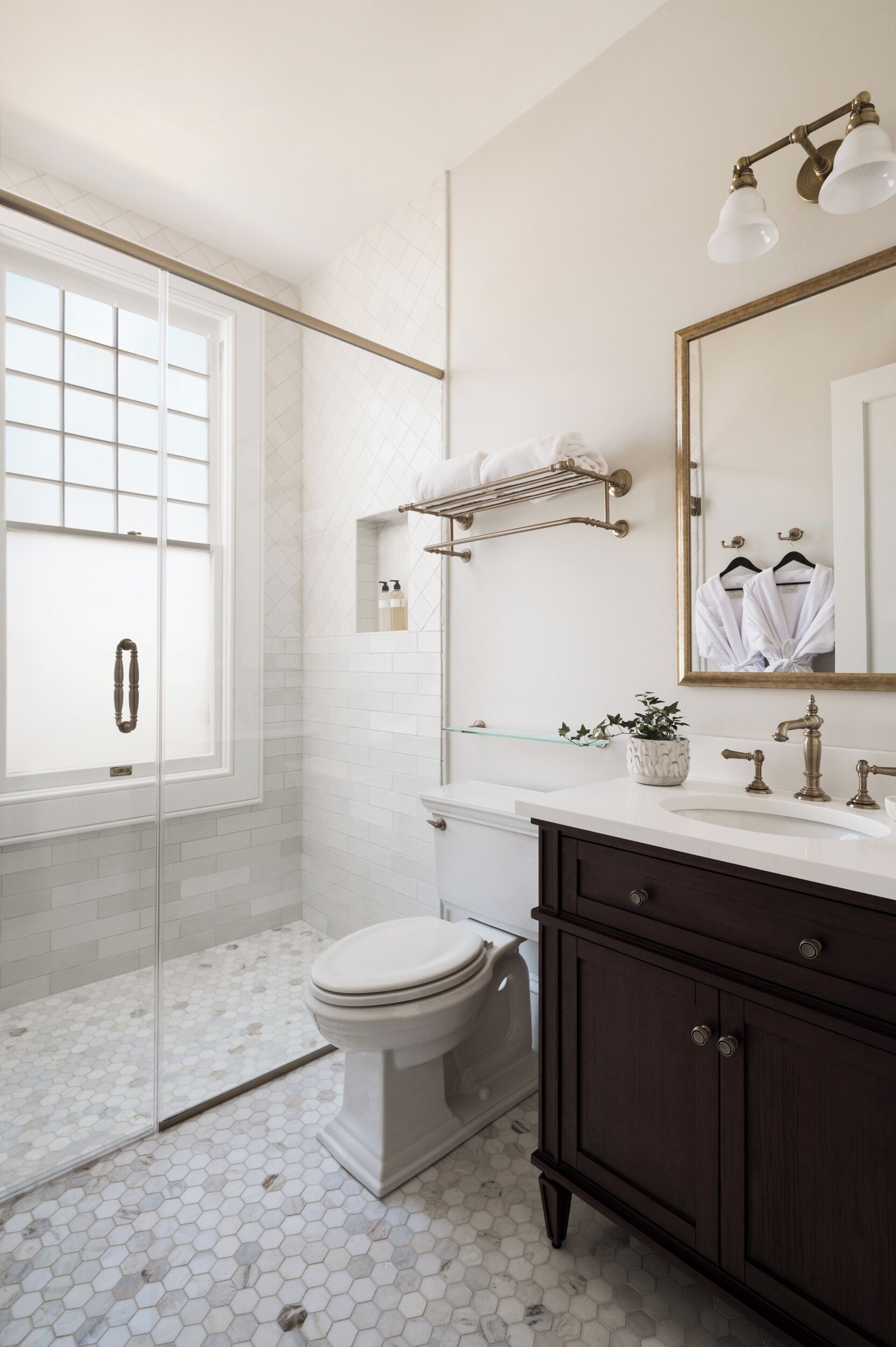 A bathroom with a glass shower door, a toilet, a sink with a mirror, and a dark wooden cabinet.