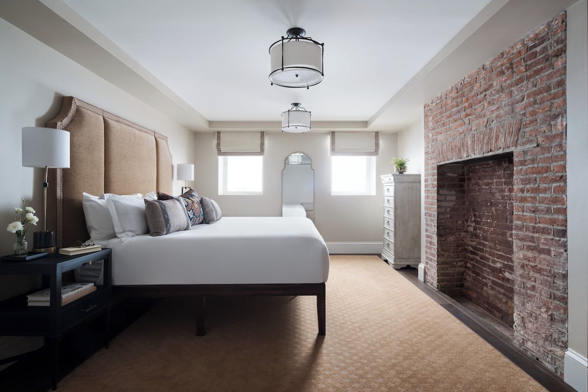 Une chambre à coucher avec un grand lit, une table de chevet, une commode, une cheminée en briques et un luminaire au plafond.