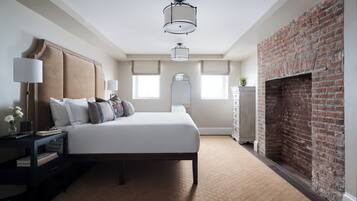 A bedroom with a large bed, a nightstand, a dresser, a brick fireplace, and a ceiling light fixture.