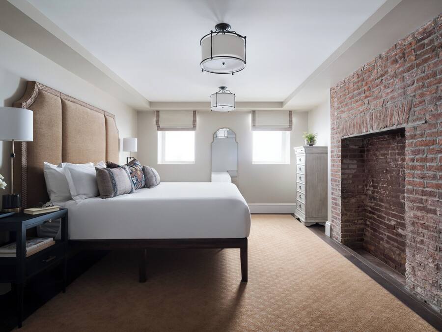 A bedroom with a large bed, a nightstand, a dresser, a brick fireplace, and a ceiling light fixture.