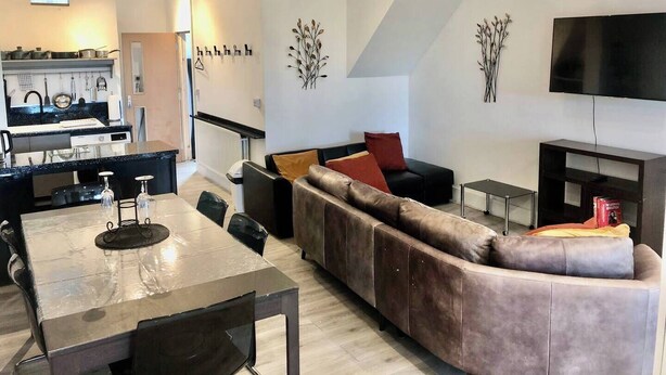 Ein modernes Apartment mit Essbereich, Küche, Wohnzimmer und einem an der Wand befestigten Fernseher.