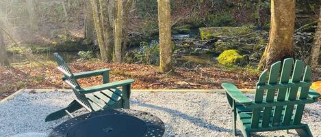 A circular outdoor seating area with two green Adirondack chairs and a round table.