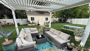 A covered patio area with outdoor furniture, including a sofa and a coffee table, surrounded by potted plants and a decorative rug. - Heber Valley Base Camp: convenient location, modern amenities, pleasant spaces (Heber City)