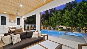 A modern outdoor living area with a pool, wooden ceiling, and a view of trees. - LUXE: Custom Beach Home w/Pool&Spa, Fire Pit, BBQ (Naples)