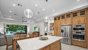 A modern kitchen with wooden cabinets, stainless steel appliances, and a central island. - LUXE: Custom Beach Home w/Pool&Spa, Fire Pit, BBQ (Naples)