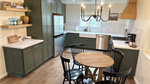 A modern kitchen with dark green cabinets, a stainless steel refrigerator, a wooden dining table with chairs, and a chandelier. - Serene Retreat Near Downtown (Prescott)