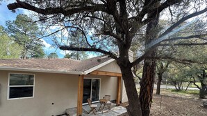 A single-story house with a covered porch, a small patio area, and a large tree in front. - Serene Retreat Near Downtown (Prescott)